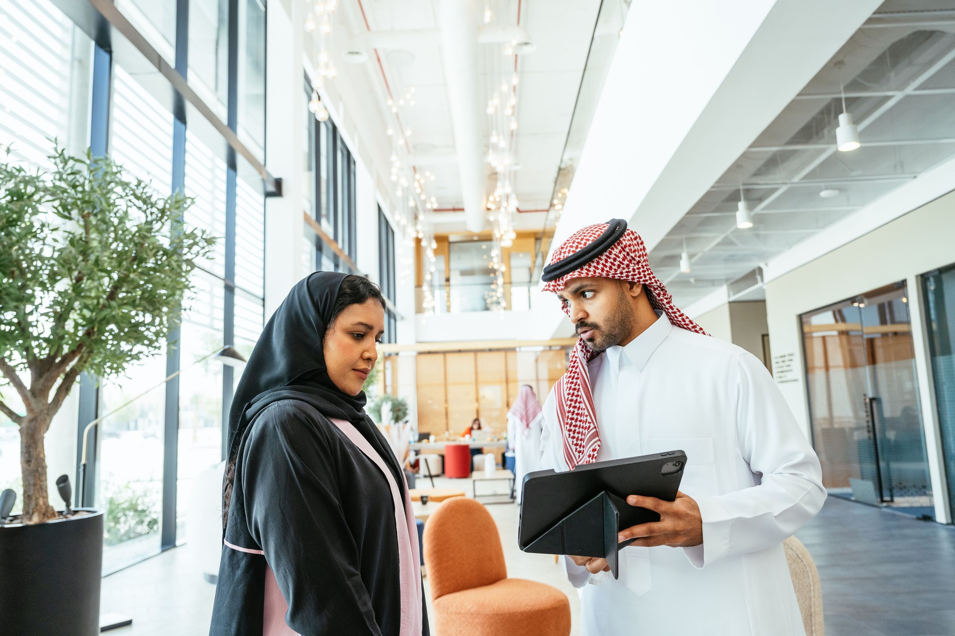 Diverse Arab business people wearing headscarfs and thawbs working together in modern bright office space using digital tablet during briefing